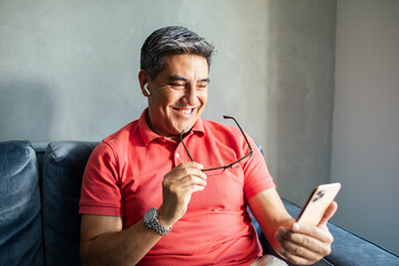 MIddle aged latin man using a smart phone on a couch at home