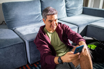 Fototapeta premium Middle aged latin man using a smart phone before going on a workout at home