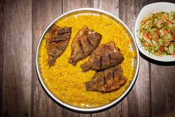 Fried fish with rice in a plate on a wooden table With Green Salad Plate beside it .
