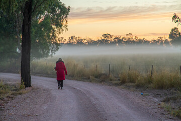 Woman in red coat walks along dusty road next to a temperature inversion in the Australian...