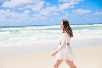 Fototapeta na wymiar 海辺を歩く白いドレスの白人の少女の後ろ姿