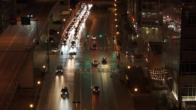 Aerial rising shot of traffic in urban city in USA at traffic light at night. Headlights and taillights illuminate street in downtown.