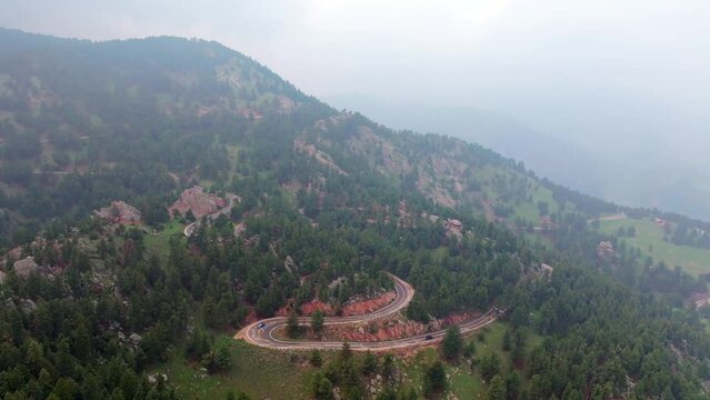 Aerial establishing shot of car driving on winding road in Rocky Mountains.