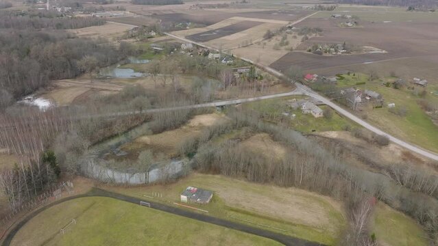 Aerial establishing view of high water in springtime, flood, Durbe river (Latvia), Cirava city, brown and muddy water, sunny day, wide drone shot moving forward, tilt down