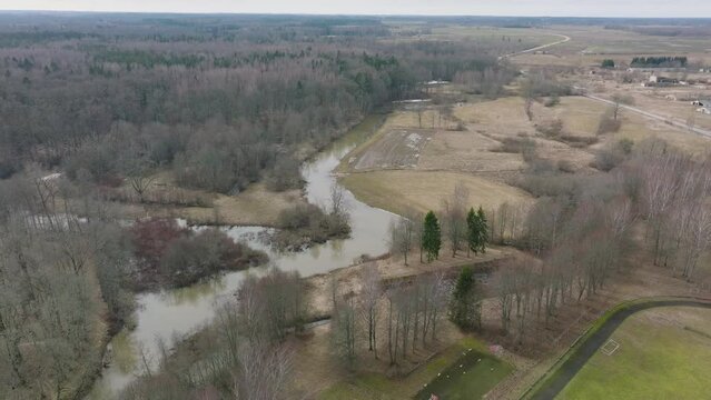 Aerial establishing view of high water in springtime, flood, Durbe river (Latvia), Cirava city, brown and muddy water, sunny day, wide drone shot moving forward, tilt down