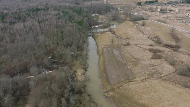 Aerial establishing view of high water in springtime, flood, Durbe river (Latvia), Cirava city, brown and muddy water, sunny day, wide drone shot moving backward