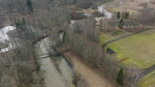 Aerial establishing view of high water in springtime, flood, Durbe river (Latvia), Cirava city, brown and muddy water, sunny day, wide drone shot moving forward, tilt up