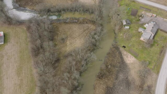 Aerial birdseye view of high water in springtime, flood, Durbe river (Latvia), Cirava city, brown and muddy water, sunny day, wide drone shot moving forward