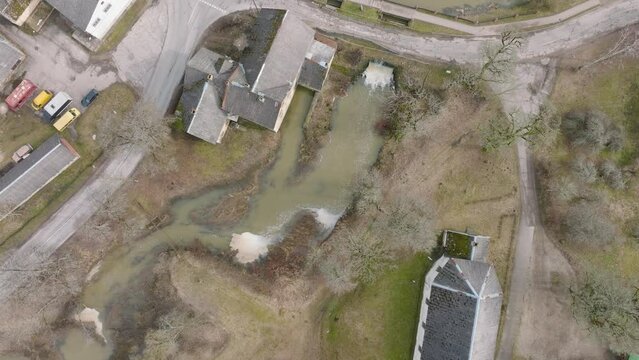 Aerial birdseye  view of high water in springtime, flood, Durbe river (Latvia), Cirava city, brown and muddy water, sunny day, wide drone shot moving forward over the rooftops