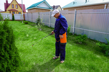 A man works in the garden, spraying weeds from a sprayer.