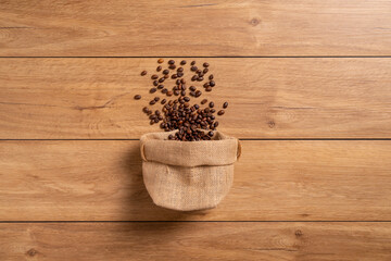 The many coffee beans are placed around on a wooden table in a warm, light atmosphere, on dark background, with copy space.