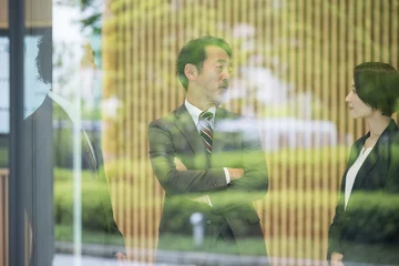 Fotobehang 窓ガラスに映りこむ立ち話をすると腕を組む社長　複数のビジネスマンたち © kapinon