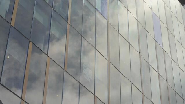 Moving clouds being shown on the windows of a large glassed building