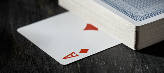 The ace of diamonds is under deck of cards on a wooden table.