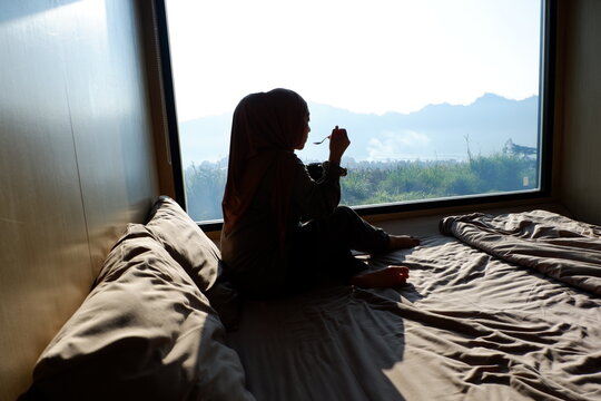 Asian hijab woman is drinking while gazing at the view from the glass window. Selective focus