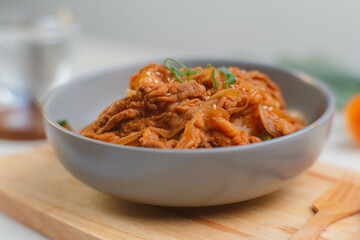 Fried kimchi with kurobuta pork on cooked rice in a bowl on wooden background. Korean food