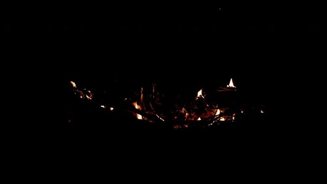 Slow motion of small flames and smoldering wood in the fire pit while burning wood at night.