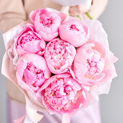 A bouquet of pink peonies in women's hands. Flower delivery. A beautiful bouquet of flowers as a gift for a holiday.