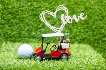 Red golf cart with ball and LOVE sign on green grass.