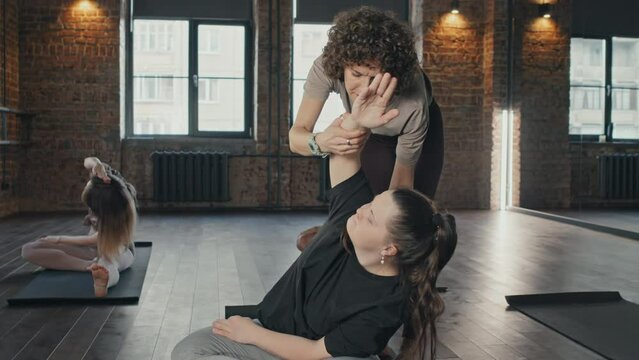 Selective focus shot of professional yoga trainer helping young woman with Down syndrome to do stretching exercise correctly