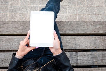 Mockup image of woman holding and using white tablet pc with blank white desktop screen while sitting on the wooden bench.Top view.Closeup.