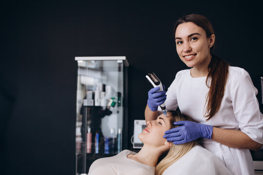 Close up of beautician hands in sterile gloves using dermapen during skincare procedure. Young woman receiving facial treatment in beauty salon. Concept of skincare and collagen induction therapy