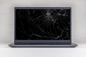 laptop pc with a broken screen in cracks on a gray background close up front view