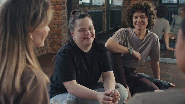 Over-the-shoulder shot of young woman with disability and her friends sitting on floor having fun while relaxing after fitness workout