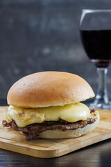 Barros Luco sandwich popular in Chile: beef with melted cheese, glass of red wine, on black table and vertical wooden table, with copy space concept of typical Chilean food