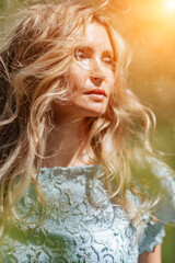 Blond garden. Portrait of a blonde in the park. Happy woman with long blond hair in a blue dress.