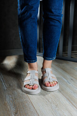Beautiful slender female legs in leather sandals on the floor against gray parquet. Collection of women's sandals