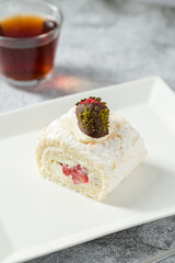 Strawberry roll cake with tea next to it on stone table