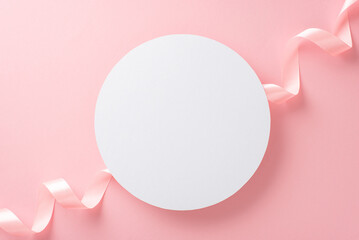 Top view photo of empty white circle with a pastel pink ribbon on an isolated light pink background with copyspace