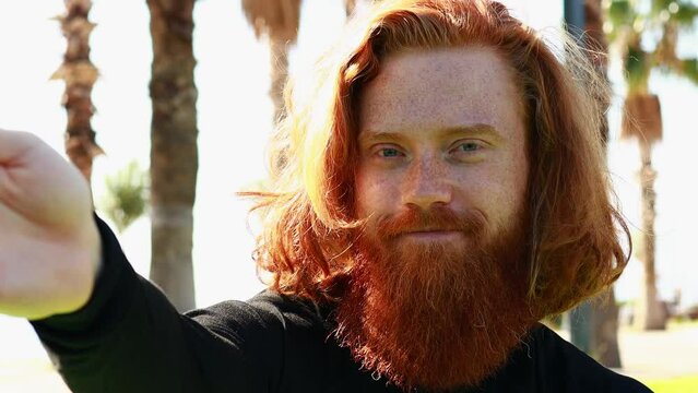 handsome redhaireb man with long beard wear black sporty suit talking with somebody in sunny beach