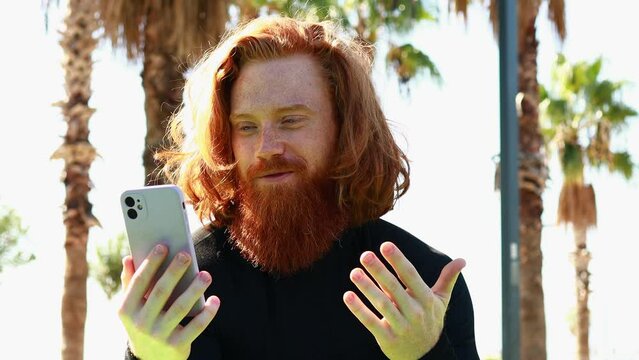 handsome redhaireb man with long beard wear black sporty suit talking with somebody in sunny beach