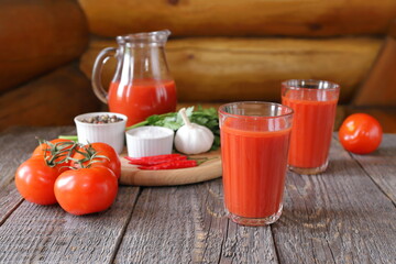 A tasty tomato juice in a glassware and fresh tomatoes with vegetables, herb and seasoning are on a wooden background.  