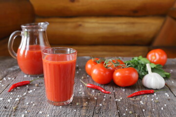 A tasty tomato juice in a glassware and fresh tomatoes with vegetables, herb and seasoning are on a...