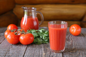 A tasty tomato juice in a glassware and fresh tomatoes with herb are on a wooden background.