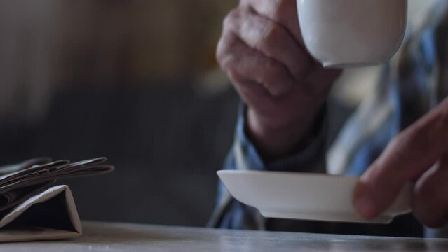 pensioner drinks delicious morning tea from a cup after reading newspapers. home leisure of an elderly person. hands of an old man holding a cup of coffee