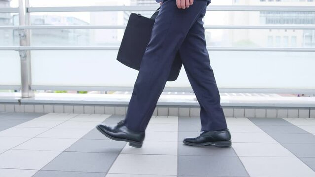 鞄を持って歩くスーツを着た若い日本人ビジネスマンの足元