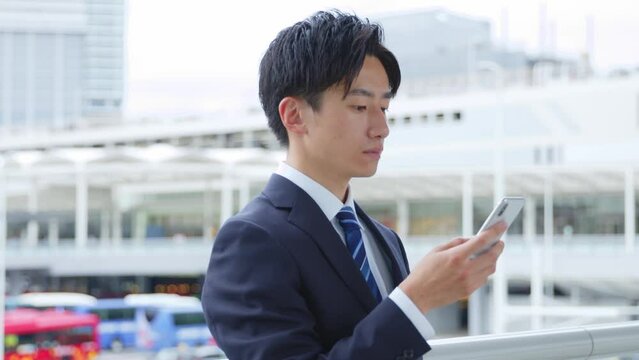 駅にてスマートフォンを使用して就職活動を行うスーツを着た若い日本人大学生