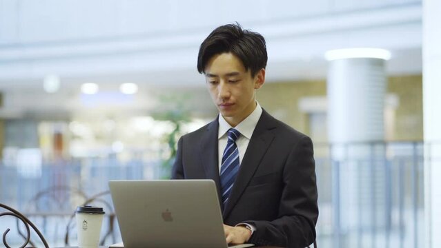 カフェでノートパソコンを使用してリモートワークをするスーツを着た若い日本人ビジネスマン