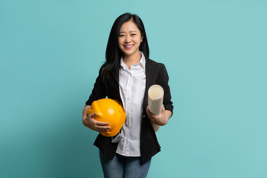 Smiling constructor worker Asian woman with clipchart and safety suit standing isolated on green background.