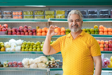 Senior indian man showing orange fruit at fruit shop. Healthy lifestyle concept.