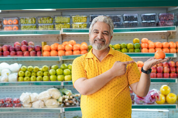 Fototapeta premium Senior indian man showing orange fruit at fruit shop. Healthy lifestyle concept.
