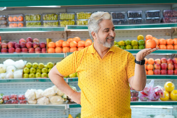 Senior indian man showing orange fruit at fruit shop. Healthy lifestyle concept.