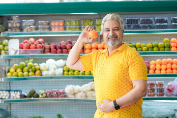 Senior indian man showing orange fruit at fruit shop. Healthy lifestyle concept.