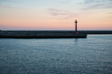 The lighthouse at harbor with some clouds in golden hour. The quite beautiful pink tone sunset at Tainan quigu of Taiwan. The sky had fantastic hue and the sea had the wonderful reflection of light.