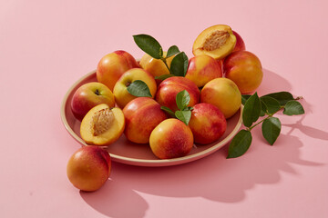 Fototapeta na wymiar Against the pastel pink background, a dish of some peaches is displayed. Peach (Prunus persica) helps enhance health condition with vitamin A and C