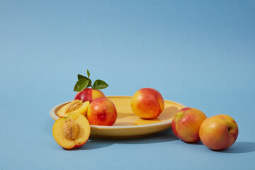 Against a blue background, fresh ripe peaches (prunus persica) decorated with a round yellow plate. Regular consumption of peaches can reduce the risk of anemia and improve heart health